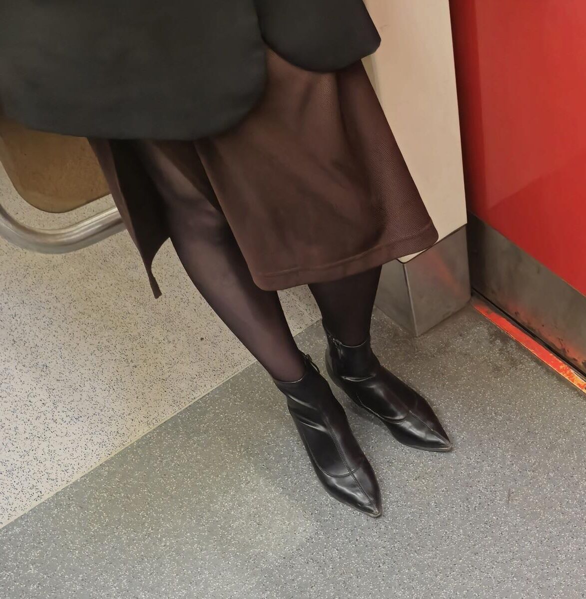 Menina de calças justas pretas, saia marrom e botas de tornozelo de couro