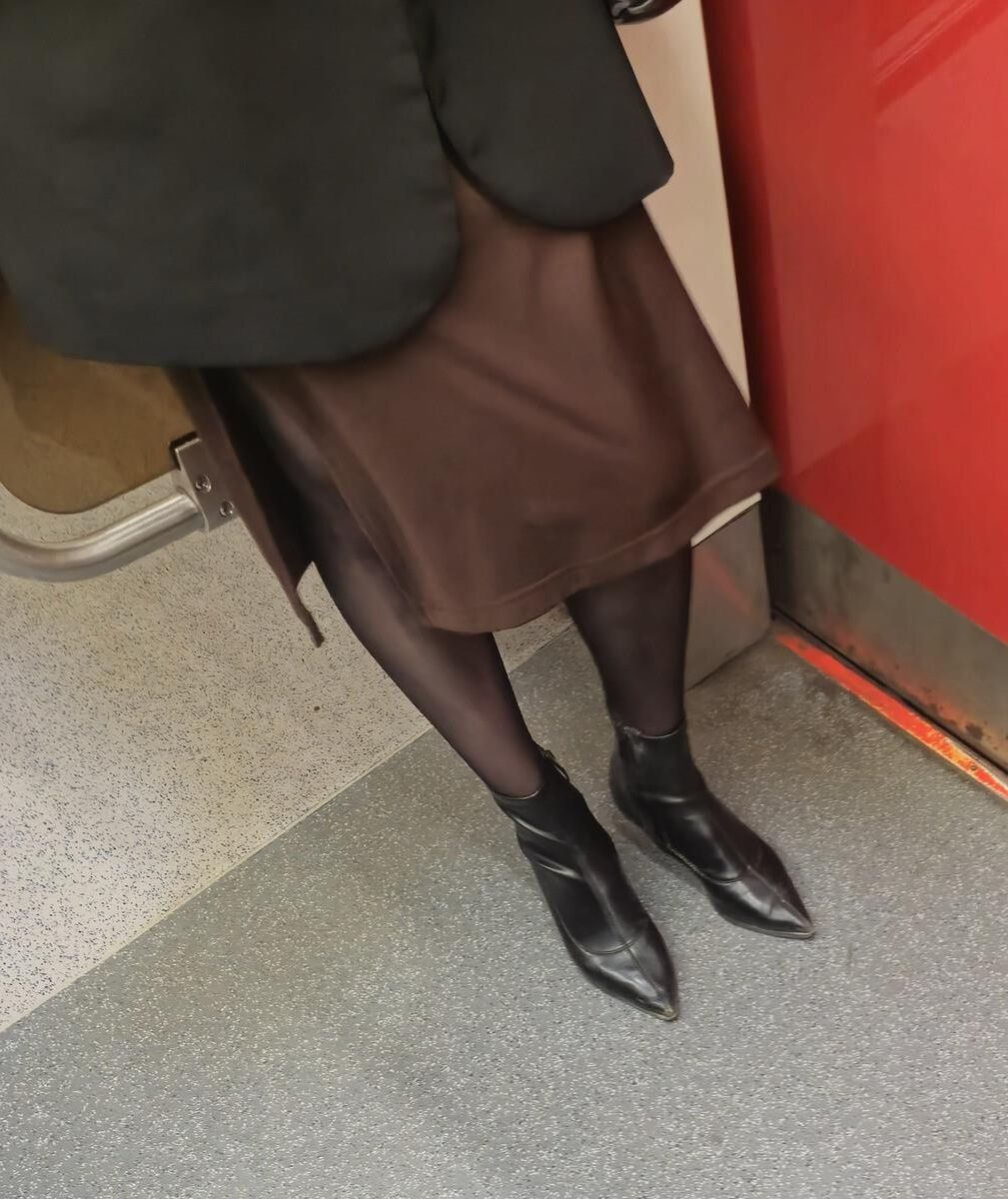 Menina de calças justas pretas, saia marrom e botas de tornozelo de couro