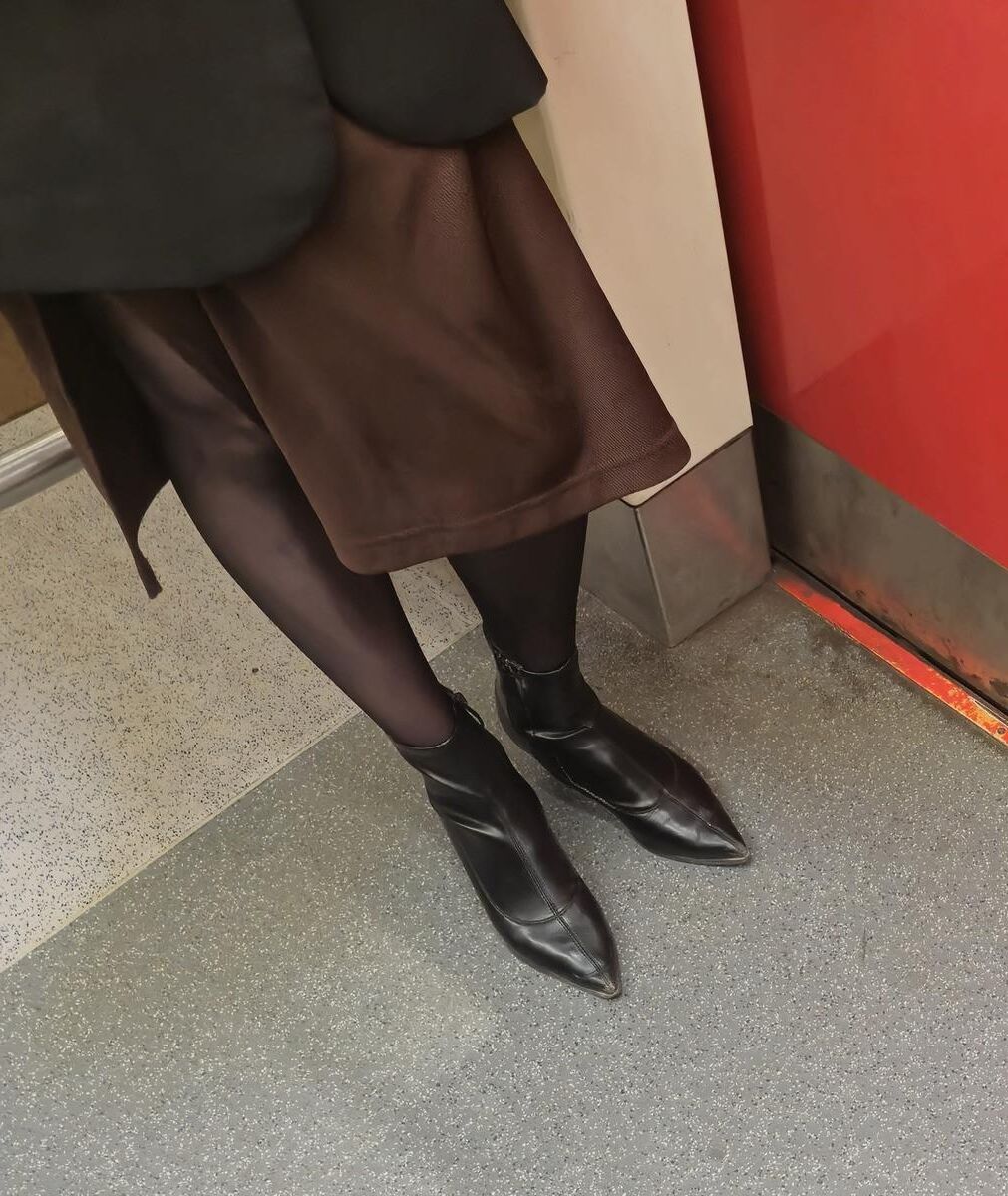 Menina de calças justas pretas, saia marrom e botas de tornozelo de couro