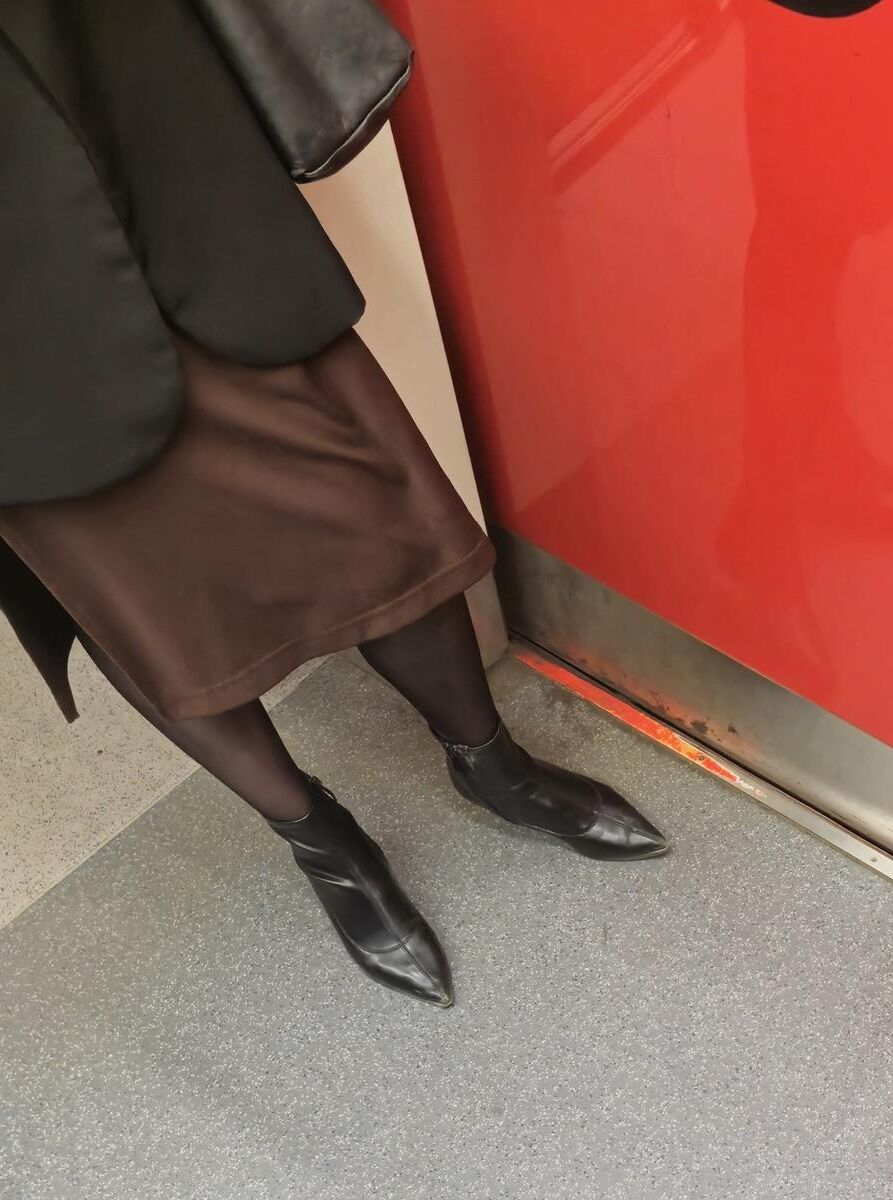 Menina de calças justas pretas, saia marrom e botas de tornozelo de couro